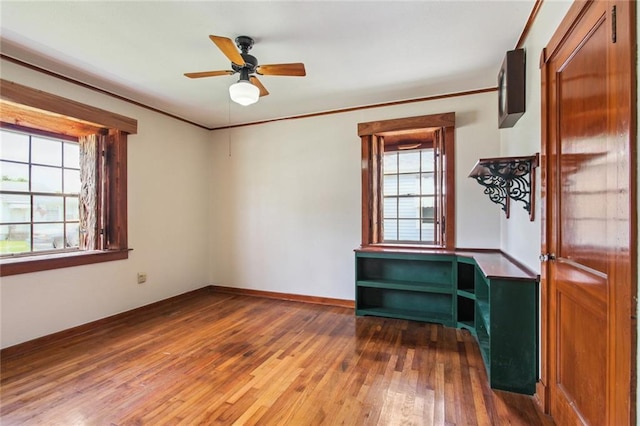 empty room featuring baseboards, wood-type flooring, ceiling fan, and crown molding