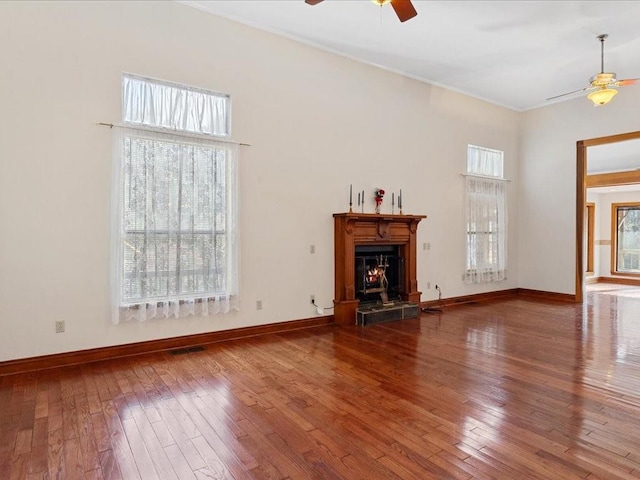 unfurnished living room featuring hardwood / wood-style floors, visible vents, a warm lit fireplace, and ceiling fan