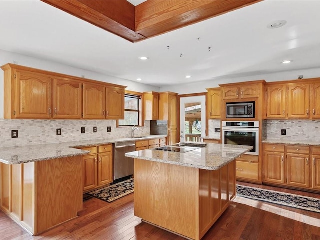 kitchen featuring a sink, a kitchen island, hardwood / wood-style floors, appliances with stainless steel finishes, and light stone countertops