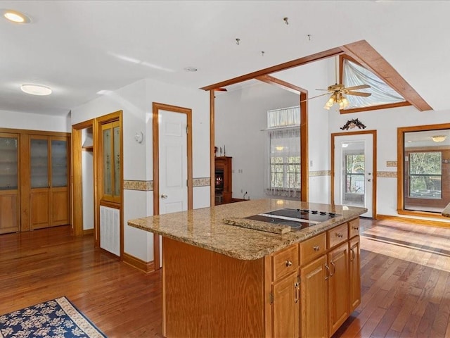 kitchen featuring light stone counters, a center island, wood-type flooring, black electric stovetop, and ceiling fan