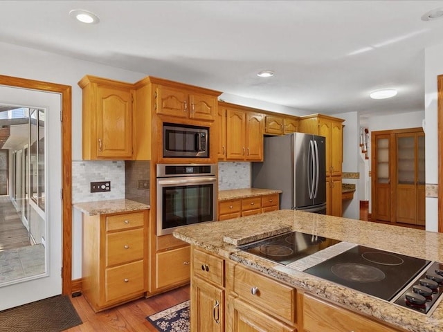 kitchen with light wood-type flooring, light stone counters, recessed lighting, appliances with stainless steel finishes, and decorative backsplash