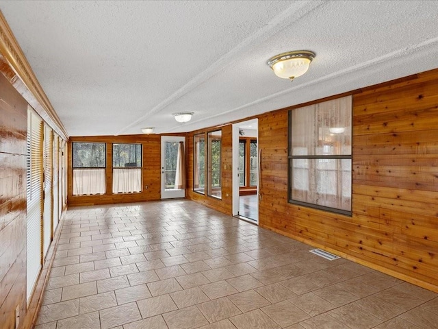 spare room with visible vents, wood walls, and a textured ceiling