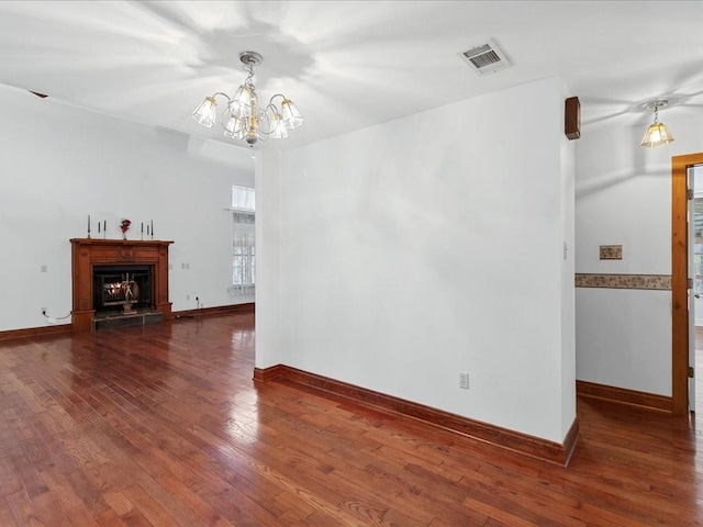 unfurnished living room featuring hardwood / wood-style floors, baseboards, visible vents, a warm lit fireplace, and a notable chandelier