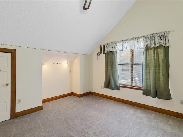 carpeted spare room featuring vaulted ceiling and baseboards