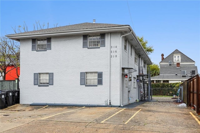 rear view of property with brick siding, uncovered parking, and fence