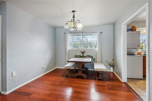 dining space with stacked washer / dryer, a chandelier, wood-type flooring, and baseboards