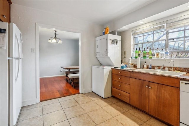 laundry room featuring estacked washer and dryer, baseboards, light tile patterned floors, and a chandelier