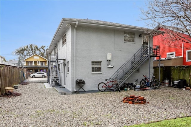 rear view of property with stairs, fence, and brick siding
