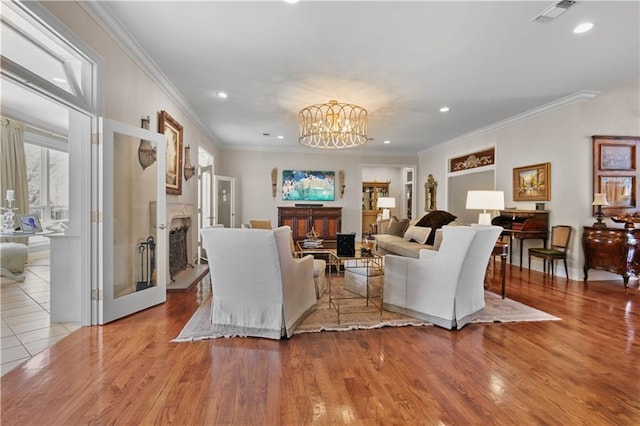 living area with wood finished floors, visible vents, a fireplace with raised hearth, ornamental molding, and a notable chandelier