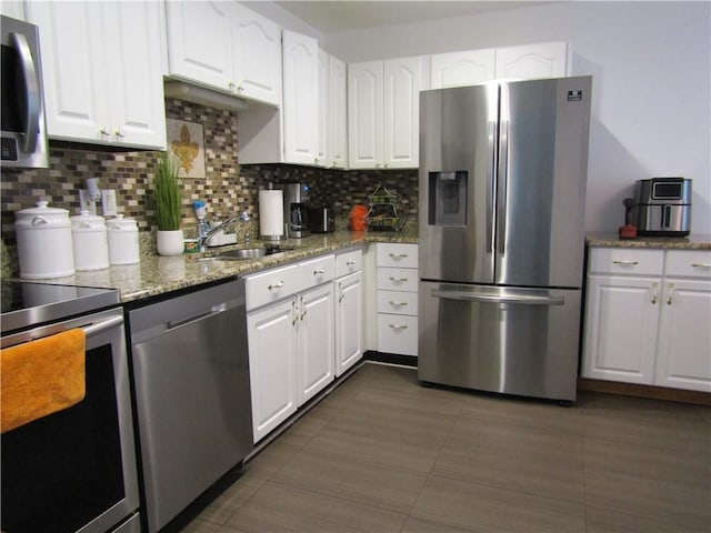 kitchen with a sink, backsplash, white cabinetry, stainless steel appliances, and light stone countertops