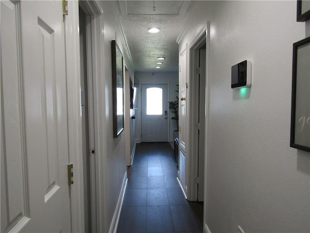 hallway with dark tile patterned floors, baseboards, and a textured ceiling