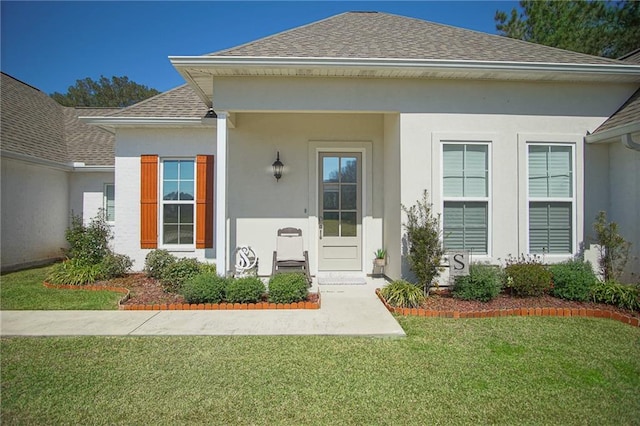 entrance to property with stucco siding, a shingled roof, and a yard