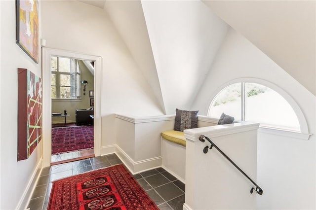 corridor with vaulted ceiling, dark tile patterned flooring, and baseboards