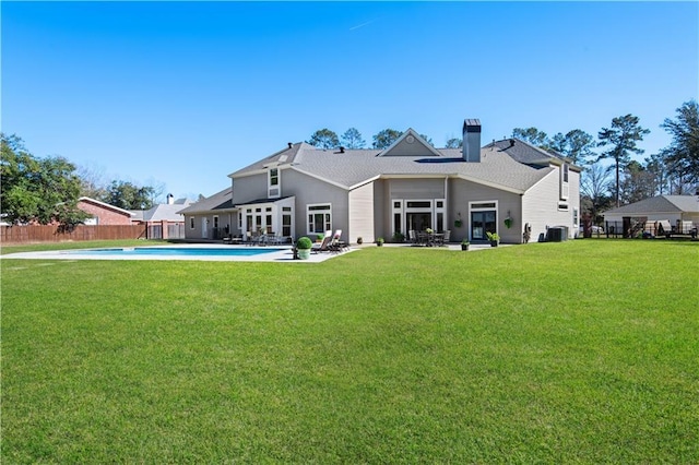 rear view of property with fence, a lawn, a fenced in pool, and a chimney