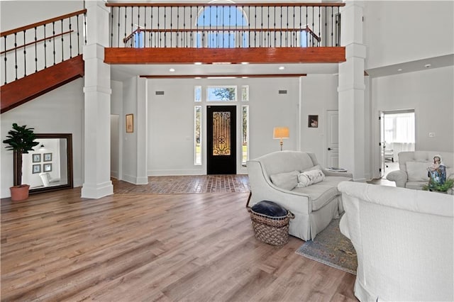 living room featuring baseboards, a high ceiling, ornate columns, and wood finished floors