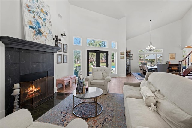 living room featuring wood finished floors, visible vents, an inviting chandelier, a high ceiling, and a tile fireplace