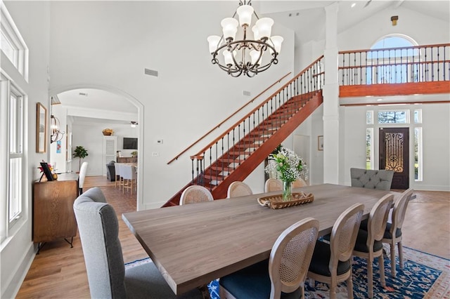 dining space featuring a wealth of natural light, light wood-type flooring, a notable chandelier, and a towering ceiling