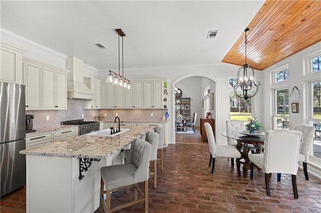 kitchen with backsplash, a chandelier, custom range hood, stainless steel appliances, and a sink