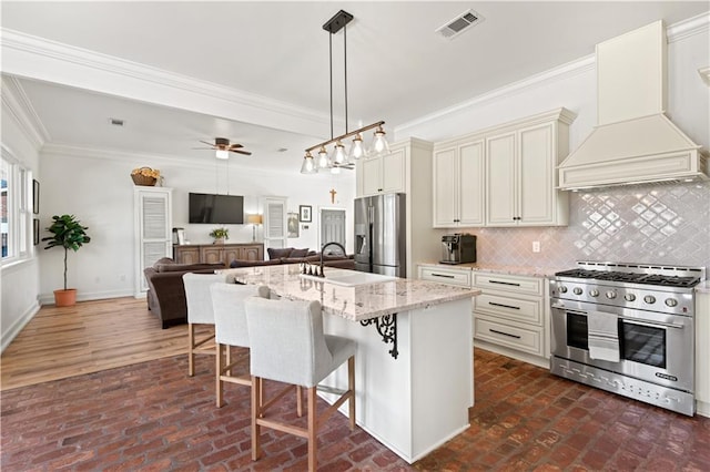 kitchen with custom range hood, a sink, open floor plan, appliances with stainless steel finishes, and light stone countertops