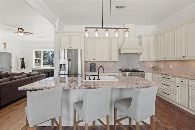 kitchen featuring a sink, stove, stainless steel refrigerator with ice dispenser, crown molding, and cream cabinets