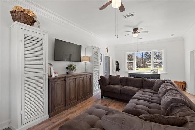 living room with light wood finished floors, visible vents, baseboards, ceiling fan, and ornamental molding