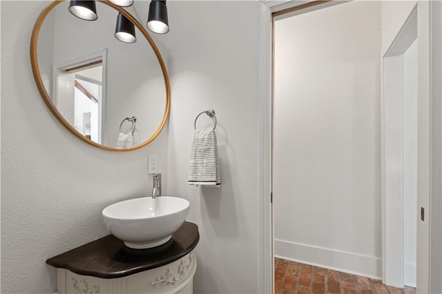 bathroom featuring brick floor, baseboards, and vanity