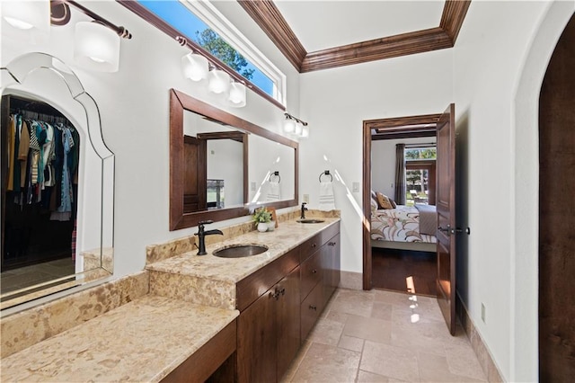 ensuite bathroom featuring a sink, double vanity, stone tile flooring, and crown molding