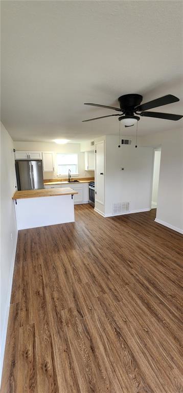 unfurnished living room featuring ceiling fan, visible vents, baseboards, and wood finished floors