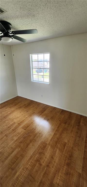 empty room with visible vents, a textured ceiling, ceiling fan, and wood finished floors