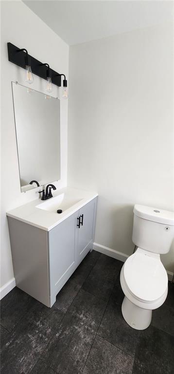 half bath with toilet, vanity, and baseboards