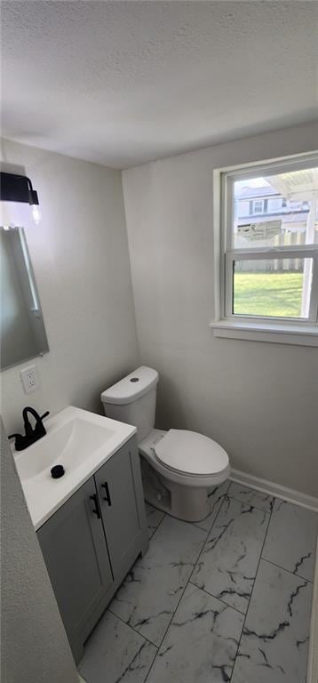 half bathroom featuring toilet, marble finish floor, vanity, and a textured ceiling