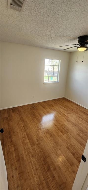 spare room featuring visible vents, a ceiling fan, a textured ceiling, wood finished floors, and baseboards