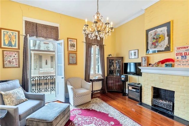 sitting room featuring a notable chandelier, ornamental molding, a fireplace, and wood finished floors