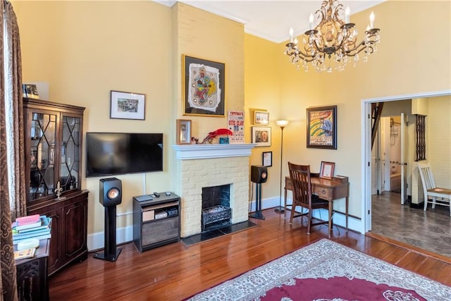 living area featuring crown molding, baseboards, hardwood / wood-style floors, a fireplace, and an inviting chandelier