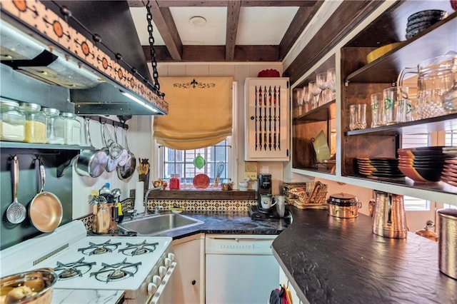 kitchen with dark countertops, under cabinet range hood, beam ceiling, white appliances, and a sink