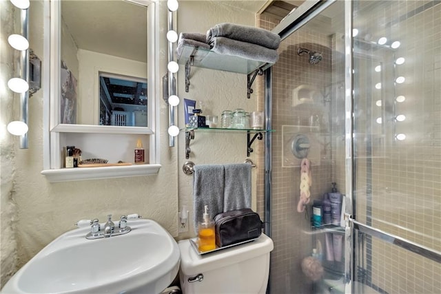 bathroom featuring a sink, toilet, a stall shower, and a textured wall