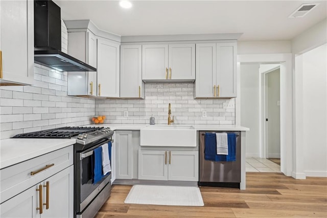 kitchen featuring a sink, light countertops, appliances with stainless steel finishes, wall chimney exhaust hood, and light wood-type flooring