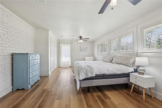 bedroom with multiple windows, wood finished floors, baseboards, and brick wall