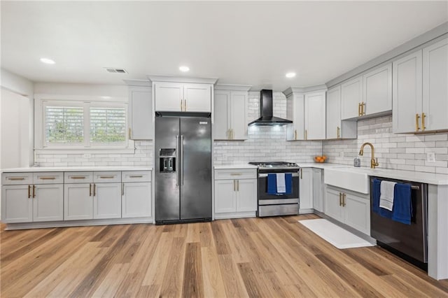 kitchen featuring light wood-type flooring, a sink, wall chimney range hood, appliances with stainless steel finishes, and light countertops