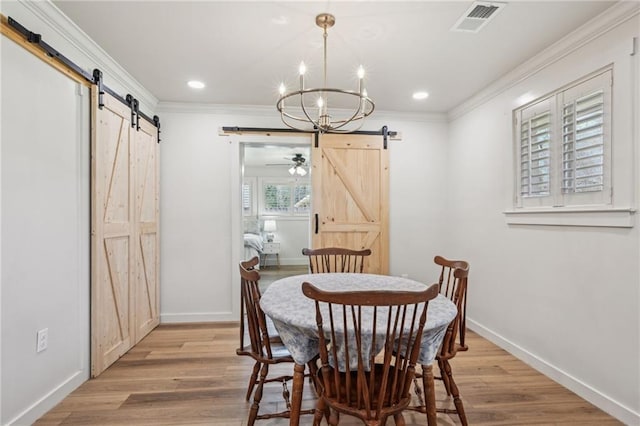 dining area featuring a barn door, light wood-style floors, visible vents, and ornamental molding