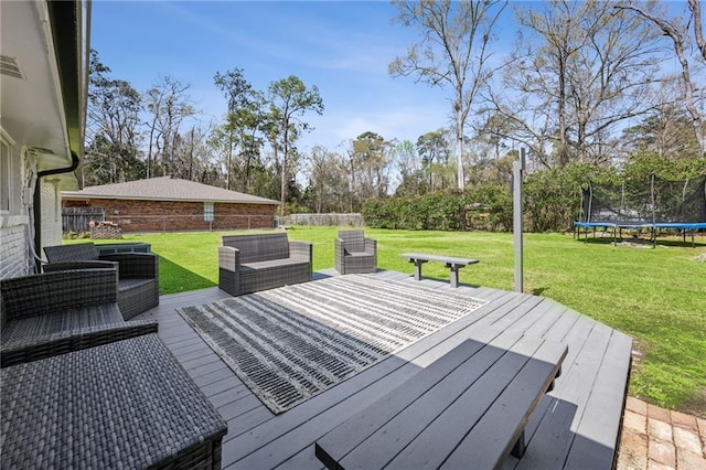 wooden deck with a yard, a trampoline, and fence