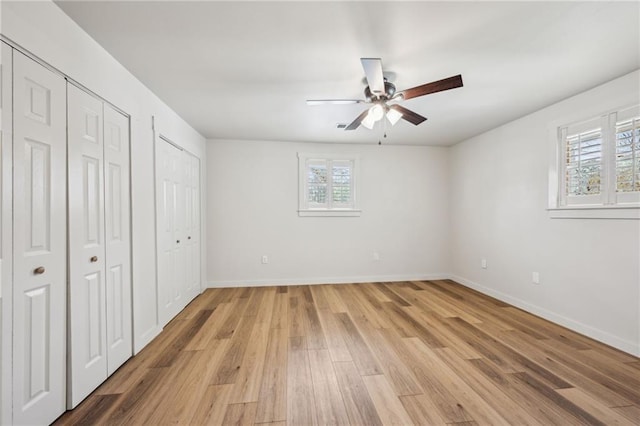 unfurnished bedroom featuring light wood finished floors, ceiling fan, two closets, and baseboards