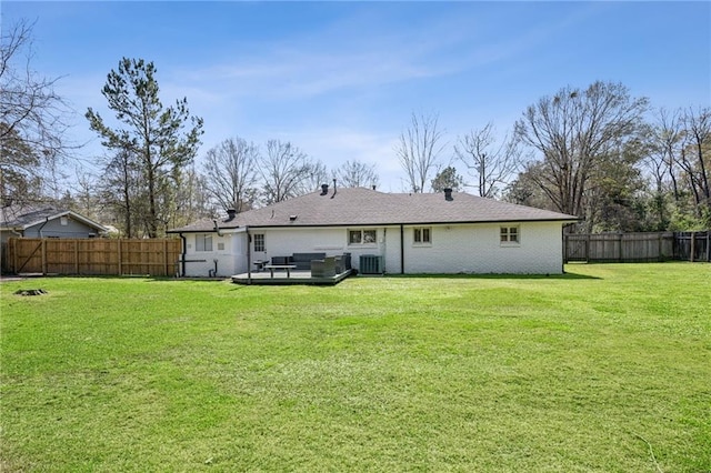 back of property with a fenced backyard, a yard, a wooden deck, brick siding, and central AC unit