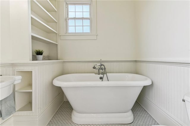 full bathroom featuring tile patterned floors, toilet, wainscoting, a decorative wall, and a freestanding bath