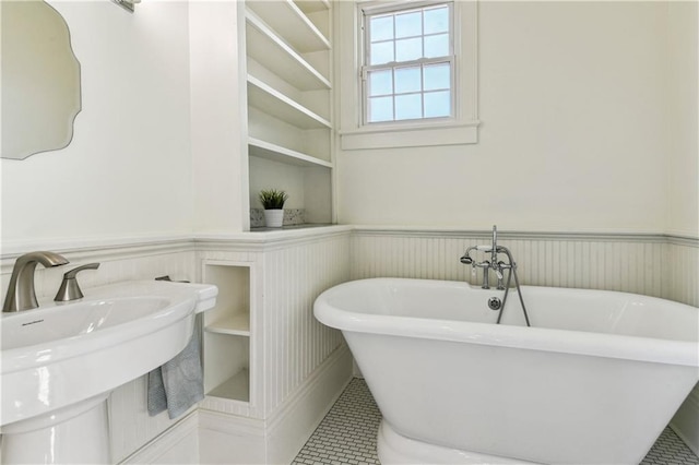 full bathroom with a sink, built in shelves, a wainscoted wall, and a freestanding bath