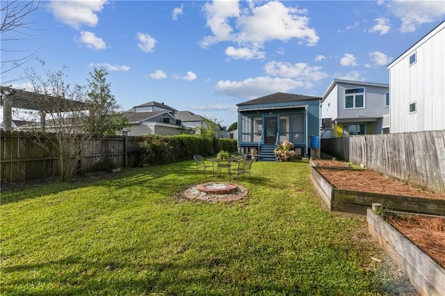 view of yard featuring a garden, an outdoor fire pit, a fenced backyard, and a sunroom