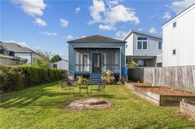 rear view of house featuring a yard, fence, a fire pit, and a sunroom