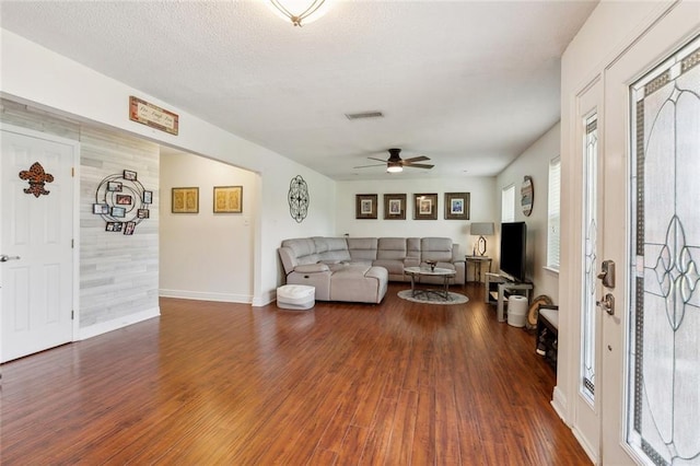 living area featuring visible vents, baseboards, dark wood finished floors, a textured ceiling, and a ceiling fan