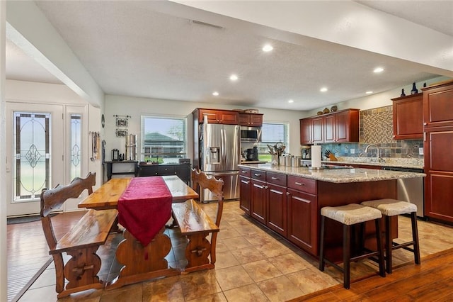 kitchen featuring reddish brown cabinets, backsplash, appliances with stainless steel finishes, and a center island