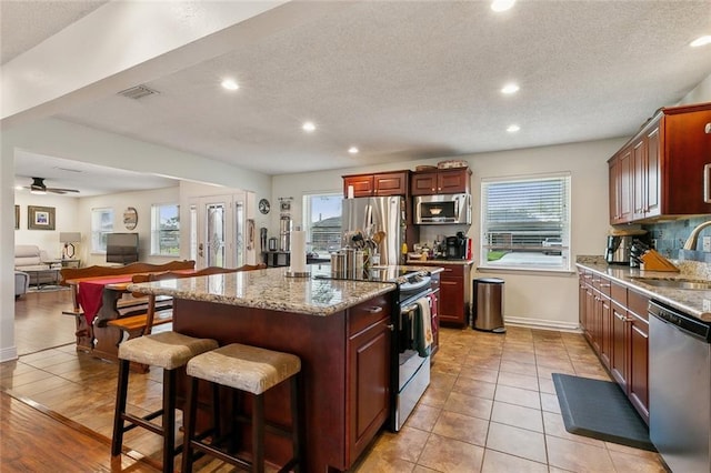 kitchen featuring visible vents, a sink, plenty of natural light, a kitchen island, and appliances with stainless steel finishes